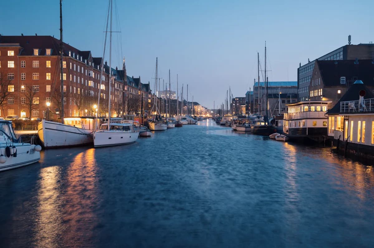 Serene night view of illuminated Nyhavn waterfront in Copenhagen with boats and historic buildings.