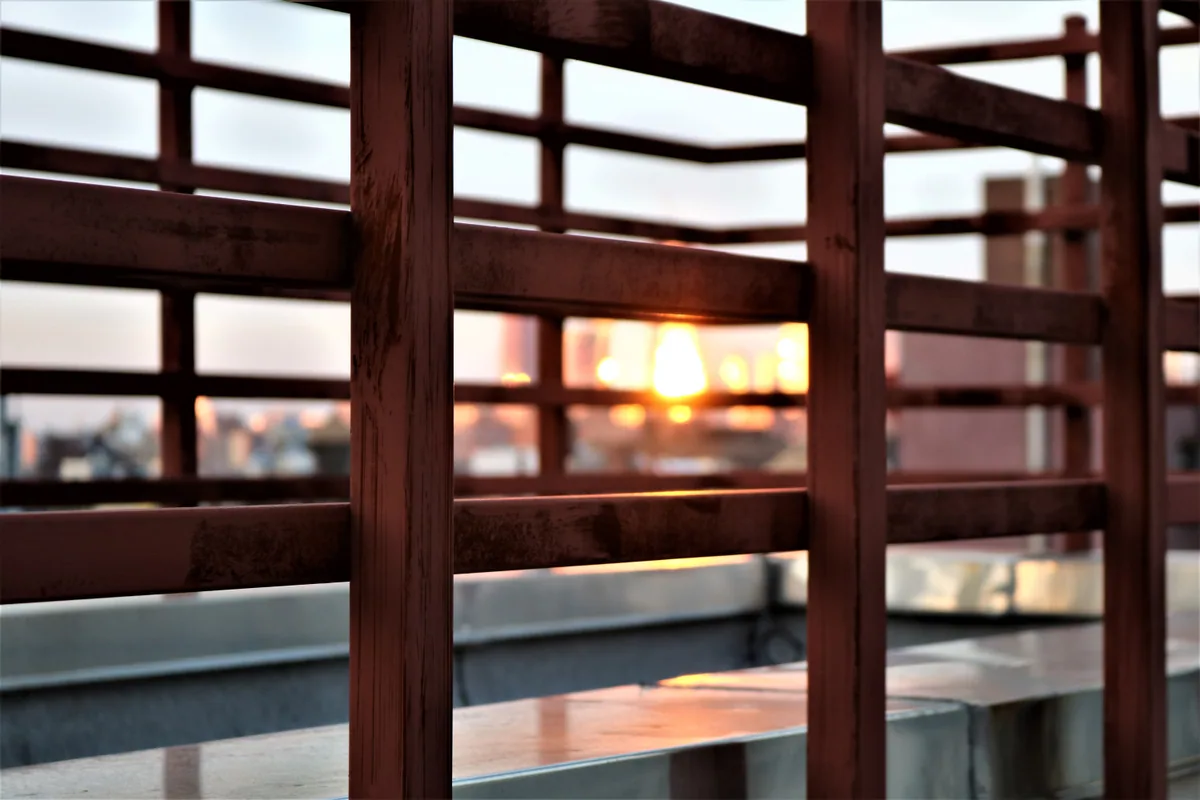 A serene view of the sunset through modern metal railings on a New York rooftop.