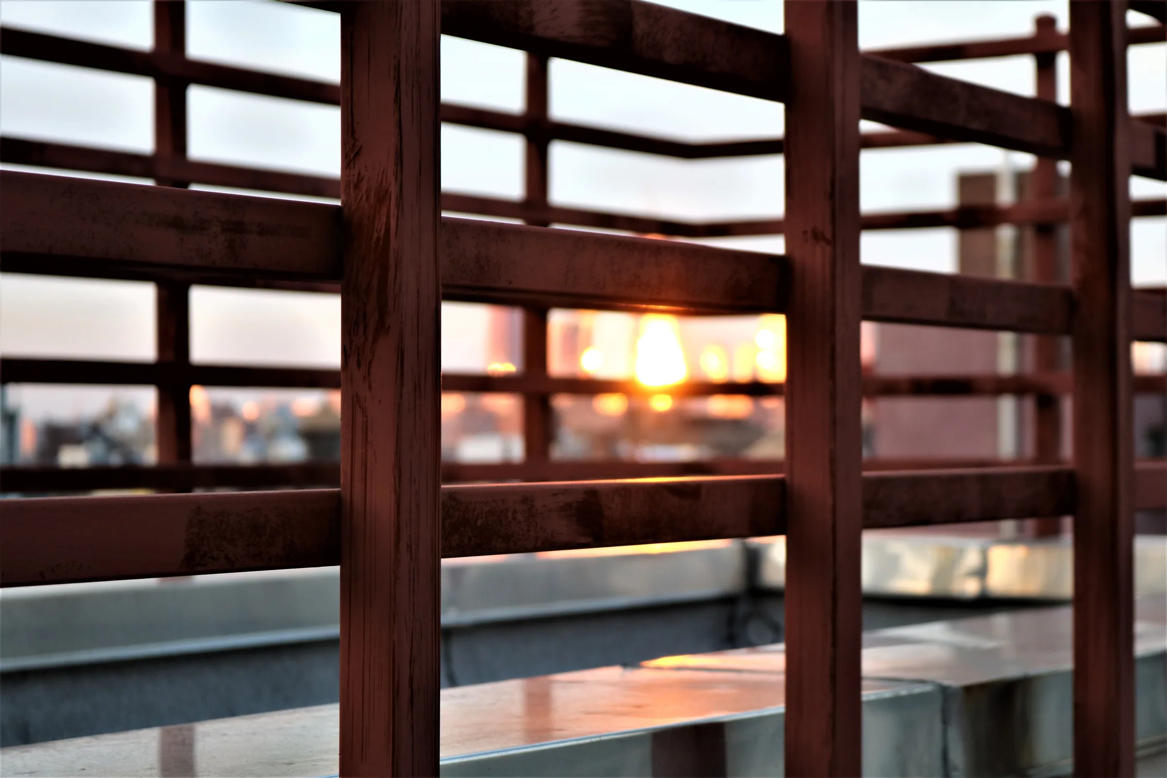 A serene view of the sunset through modern metal railings on a New York rooftop.