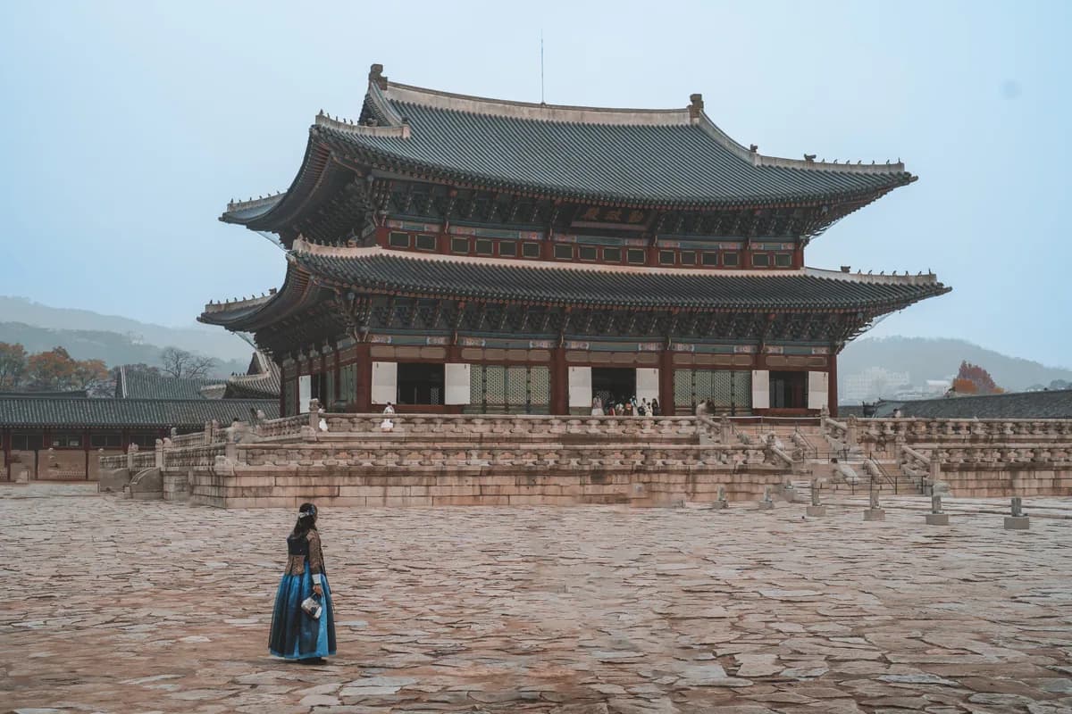 Woman in traditional hanbok attire walking past Seoul's iconic Gyeongbokgung Palace.