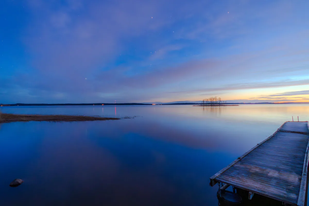 Editorial travel scenery — a still lake pier at dusk