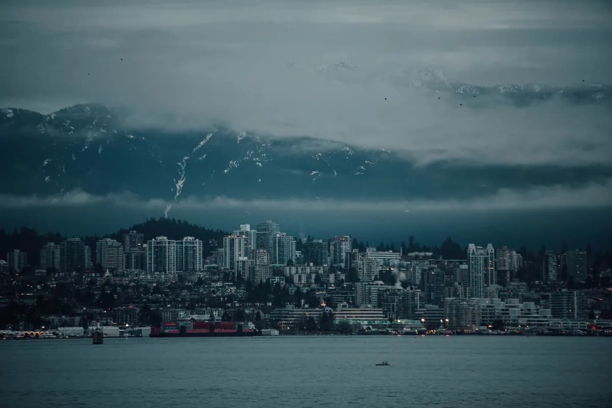 A dramatic view of Vancouver's skyline with fog-covered mountains in the background, evoking a moody ambiance.