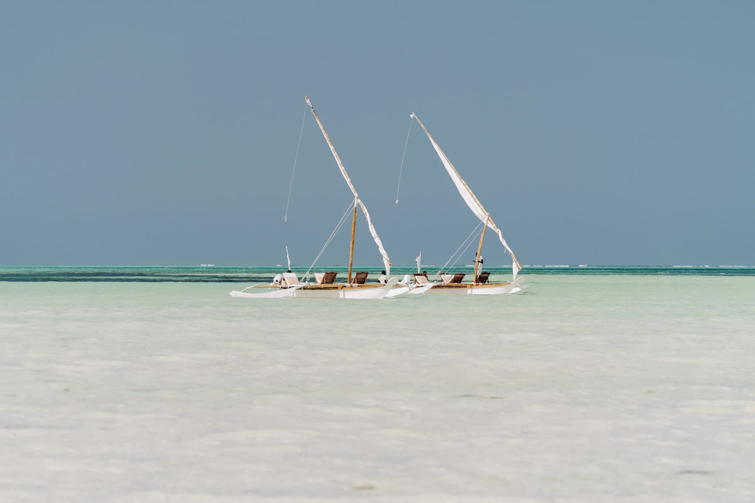 Serene scene of traditional dhows sailing on Zanzibar's turquoise waters under a clear sky.